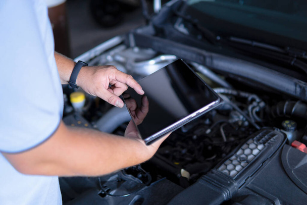 Close up view of an Auto mechanic with digital tablet at work making an engine repair diagnosis of a car in a mechanic garage - Photo, Image