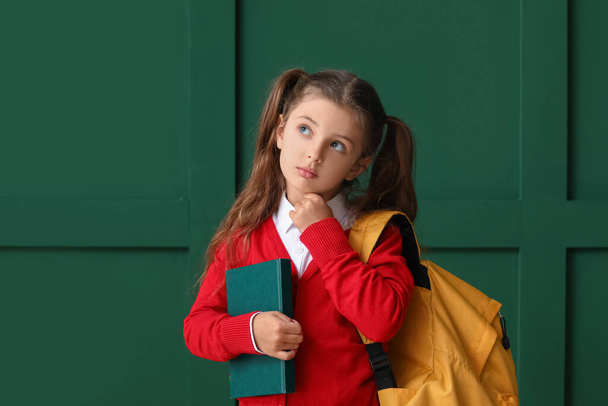 Thoughtful little school girl with book on color background - Fotó, kép