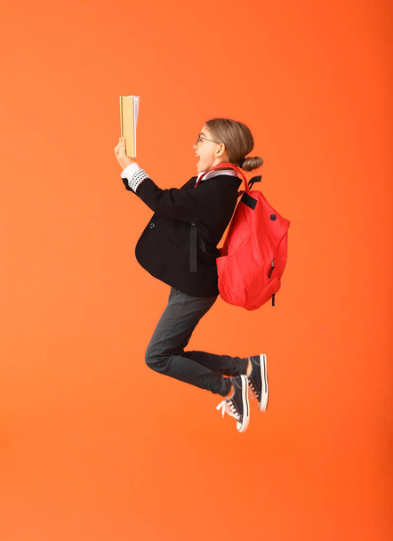 Jumping little school girl with book on color background - Zdjęcie, obraz