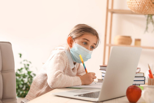 Маленька дівчинка в медичній масці навчається онлайн вдома
 - Фото, зображення