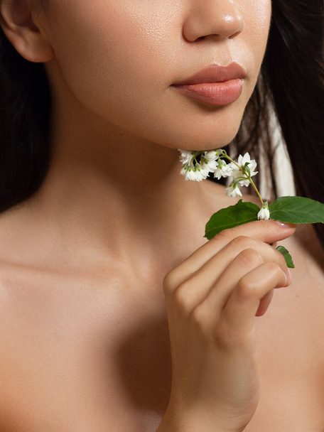 Macro photo of female lips with beautiful skin and nude makeup. light transparent gloss on full lips and white flowers. Fashion photography. Cosmetology and spa. Freshness of spring - 写真・画像