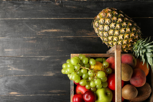 Basket with fresh fruits on dark wooden background - Photo, Image