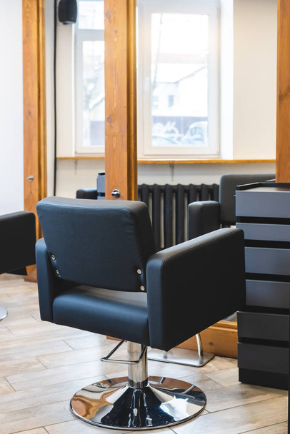 Beauty salon barbershop interior. Comfortable black leather armchairs in front of large panoramic mirrors in stylish wooden frames in a modern, cozy and bright room. - Fotó, kép
