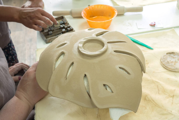 Woman hand potter making clay monstera leaf in pottery workshop studio. Process of creating ceramic vase. Handmade, hobby art and handicraft concept - Foto, imagen