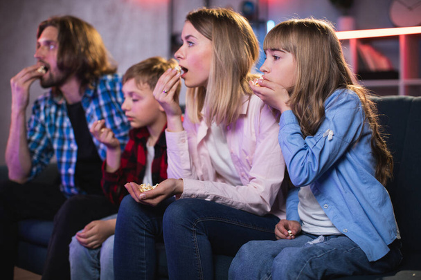 Erstaunte Eltern mit Kindern, die fernsehen und Popcorn essen - Foto, Bild