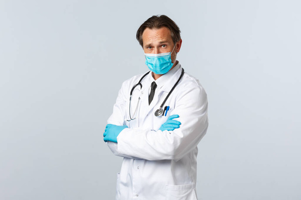 Covid-19, Prävention von Viren, Gesundheitspersonal und Impfkonzept. Vertrauensvoller professioneller Arzt, der sich um Patienten während der Coronavirus-Pandemie kümmert, Kreuzarmbrust, medizinische Maske und Handschuhe trägt - Foto, Bild