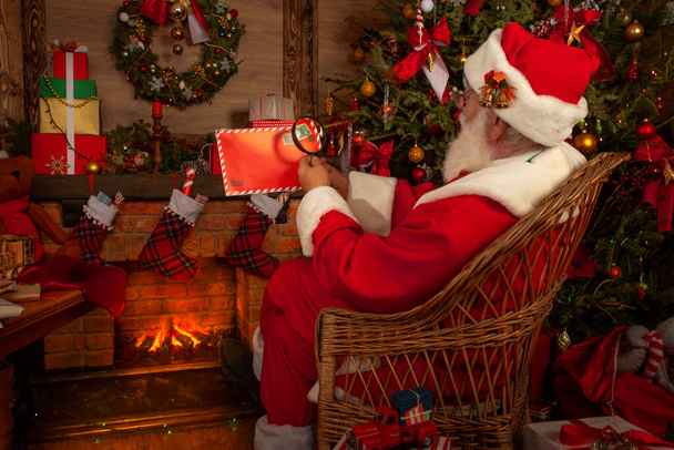 Père Noël se réjouissant avec des lettres et du courrier dans son bureau de poste à l'intérieur Log Cabin au pôle Nord. Grand-père se prépare pour la fête de Noël. Modèle senior avec barbe cosplay Père Noël - Photo, image