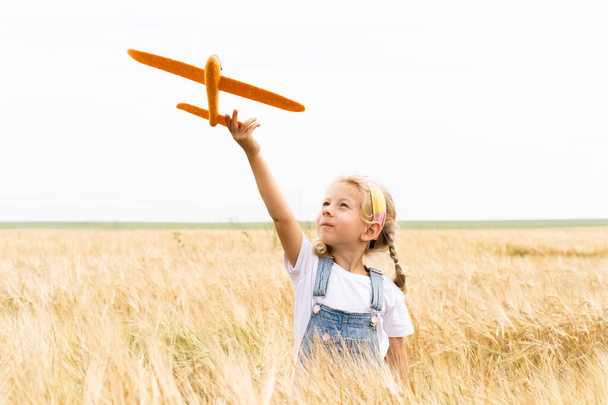 Little blonde girl plays plane in the field of rye, grain harvest - Fotó, kép
