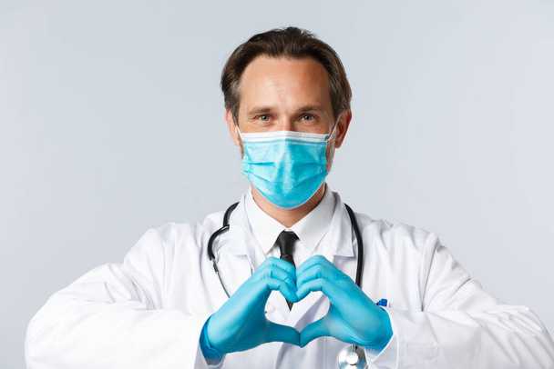 Covid-19, het voorkomen van virus, gezondheidswerkers en vaccinatie concept. Close-up van zorgzame en vriendelijke arts met medisch masker, handschoenen, zorg voor de gezondheid van de patiënt, hartklachten - Foto, afbeelding