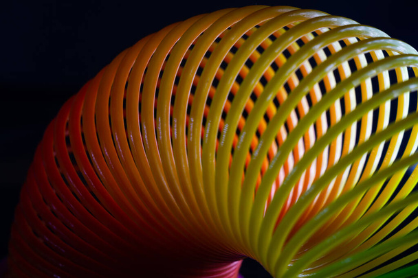 A closeup shot of a slinky rainbow spring toy on a black background - Fotó, kép