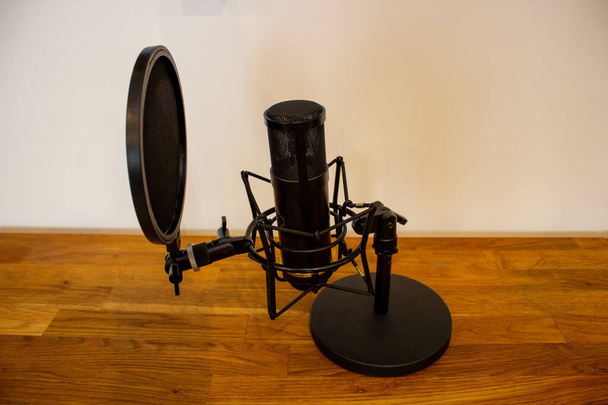 A closeup of a black professional studio condenser microphone on the wooden floor - Φωτογραφία, εικόνα