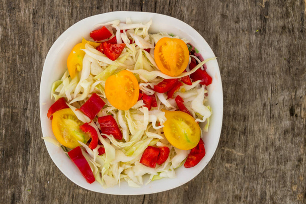 Fresh vegetable salad with cabbage, yellow tomatoes and red sweet pepper on rustic wooden table. Top view - Foto, immagini