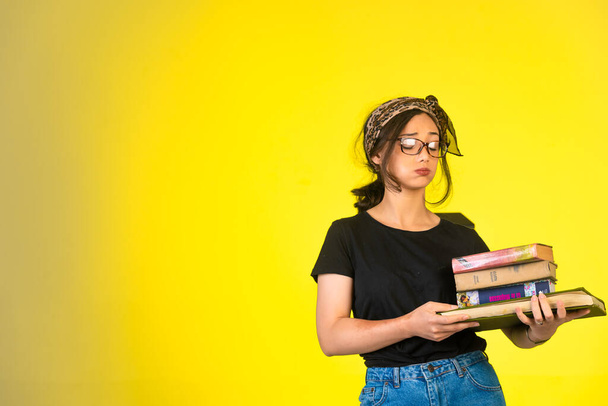 Молода школярка в окулярах тримає свої книжки і виглядає виснаженою. Високоякісна фотографія
 - Фото, зображення