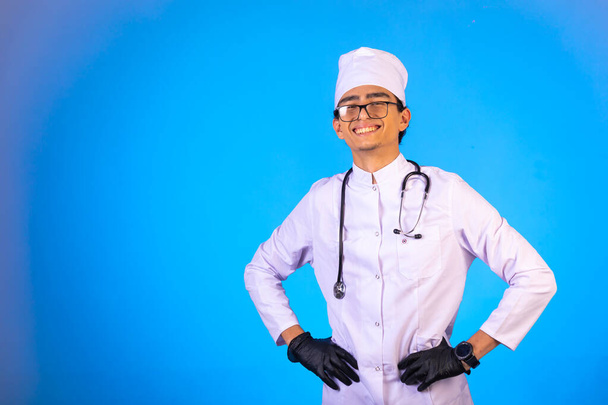 Arzt in weißer Arztuniform mit Stethoskop legte die Hände an seine Taille und lächelte. Hochwertiges Foto - Foto, Bild
