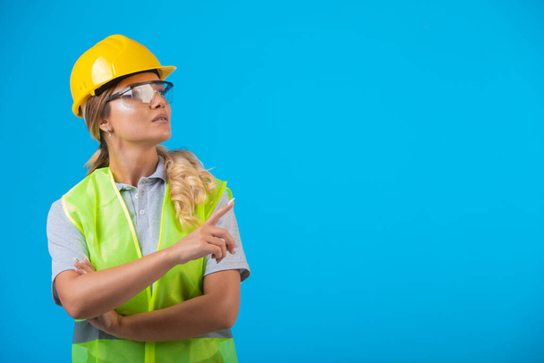 Ingénieur féminin en casque jaune et équipement portant des lunettes préventives et montrant quelque chose. Photo de haute qualité - Photo, image