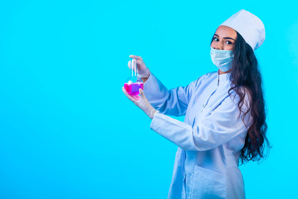 Egy fiatal nővér izolált egyenruhában, kezében egy tesztlombikkal. Kiváló minőségű fénykép - Fotó, kép