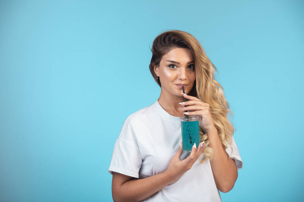 Nuori tyttö valkoisessa paidassa juo lasillisen sinistä cocktailia. Laadukas kuva - Valokuva, kuva