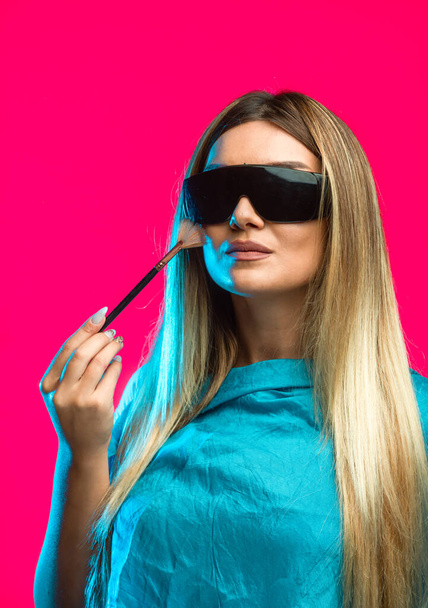Blond model wearing black sunglasses and applying cosmetics. High quality photo - Photo, Image