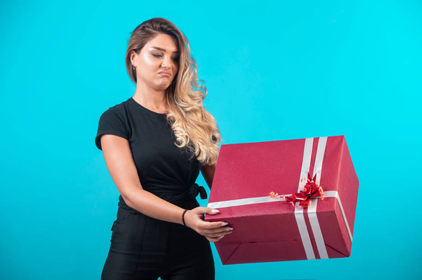 Young girl in black shirt holding a big gift box and looks confused. High quality photo - Photo, Image