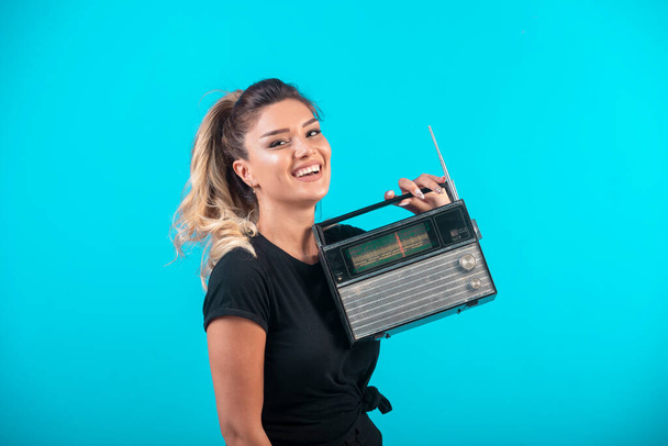 Chica joven con camisa negra sosteniendo una radio vintage y se siente positiva. Foto de alta calidad - Foto, imagen