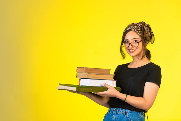 Junge Schülerin mit Brille, die ihre Bücher in der Hand hält und positiv lächelt. Hochwertiges Foto - Foto, Bild