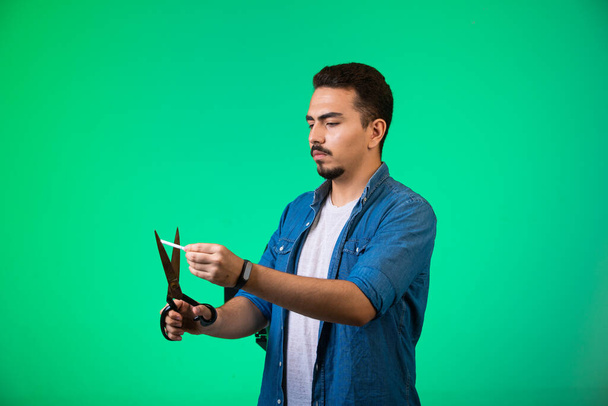 Een man die een papier knipt met een schaar op een groene achtergrond. Hoge kwaliteit foto - Foto, afbeelding