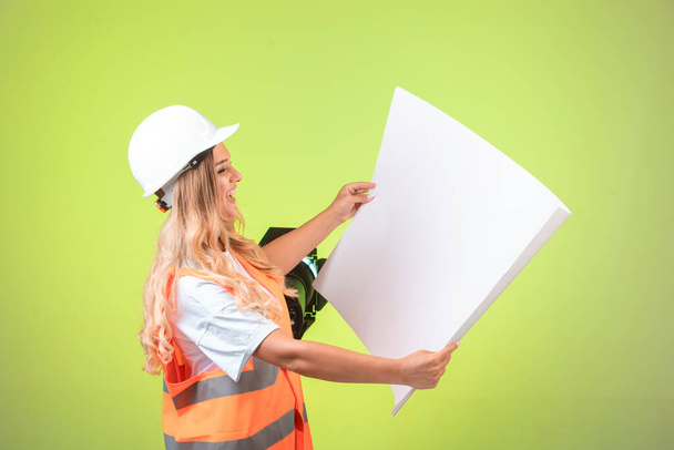 Beyaz kasklı ve teçhizatlı kadın mühendis inşaat planını tutuyor ve okuyor. Yüksek kalite fotoğraf - Fotoğraf, Görsel