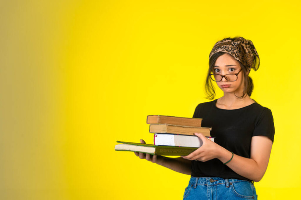 Gözlüklü genç kız kitaplarını tutuyor ve kafası karışıyor. Yüksek kalite fotoğraf - Fotoğraf, Görsel