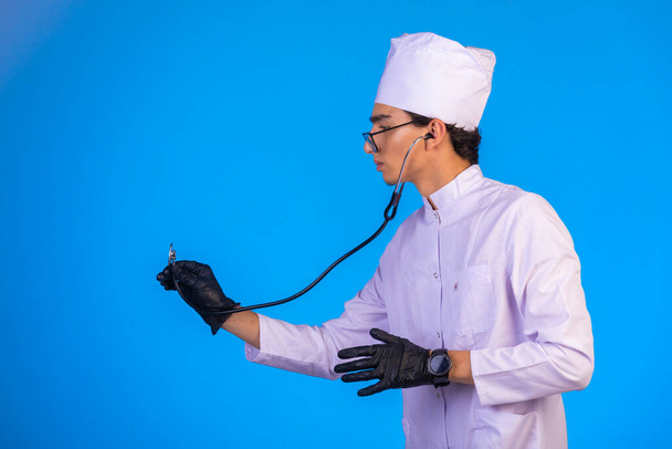 Médecin en uniforme médical blanc vérifiant avec stéthoscope masques à main sur fond bleu. Photo de haute qualité - Photo, image