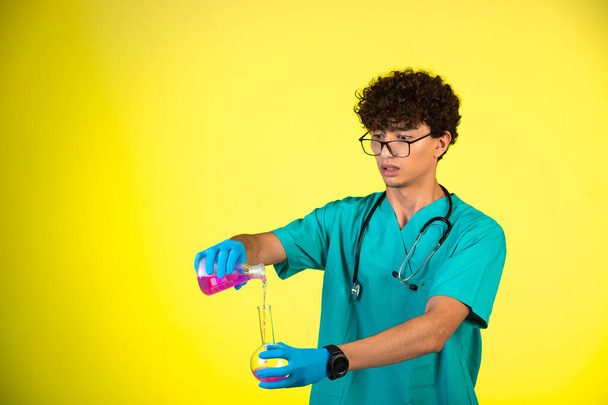 Curly hair boy in medical uniform and hand masks doing reaction with chemical liquid. High quality photo - Фото, зображення