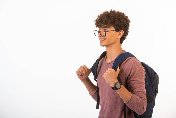 Curly hair boy in optique glasses holding his backpack is happy and joyful. High quality photo - Foto, Imagem