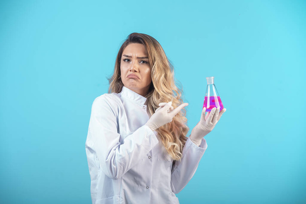 Nurse in white uniform holding a chemical flask with pink liquid and feels confused. High quality photo - 写真・画像