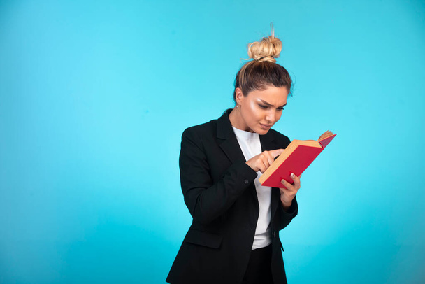 Mujer de negocios en blazer negro con un libro rojo y leerlo. Foto de alta calidad - Foto, Imagen