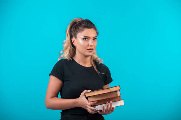 Female student holding a heavy stock of books . High quality photo - Photo, Image