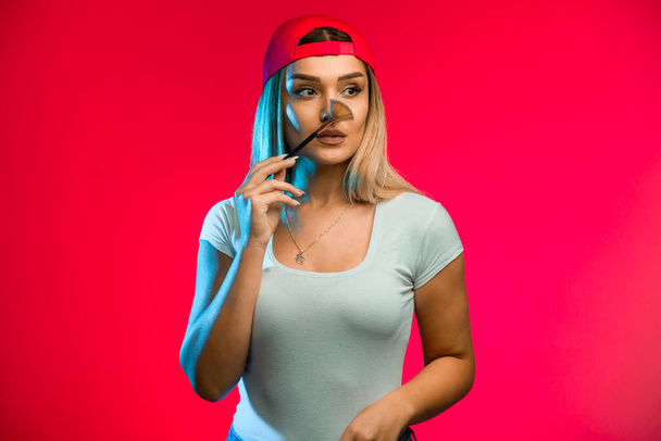 Blond model wearing red cap and applying makeup. High quality photo - Photo, Image