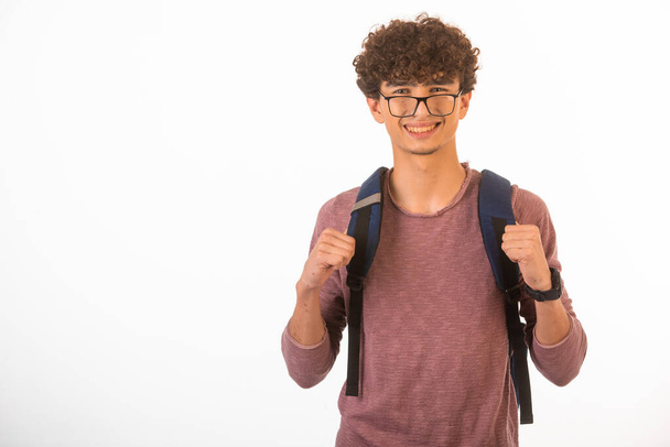 Cabello rizado niño en gafas ópticas sosteniendo su mochila y está listo para viajar. Foto de alta calidad - Foto, Imagen