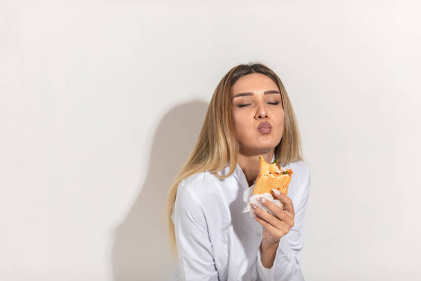 Szőke modell, aki szendvicset harap és élvezi. Kiváló minőségű fénykép - Fotó, kép