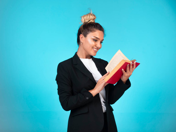 Mulher de negócios em blazer preto com um livro vermelho e lê-lo. Foto de alta qualidade - Foto, Imagem