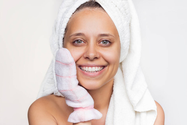 A young beautiful caucasian woman with a white towel on her head after a shower massaging her shoulder with an exfoliating hydro glove. Skin care, cosmetology - Foto, Imagem