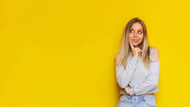 Banner. A young caucasian pretty thoughtful blonde woman thinks about something looking away at empty copy space for text or design isolated on a bright color yellow background - Foto, afbeelding