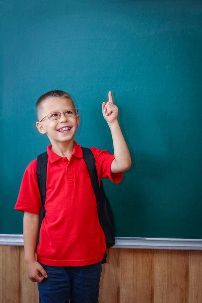 Happy child child standing at the blackboard with a school backpack wearing glasses - Foto, imagen