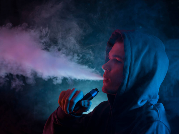Ein Mann atmet eine Wolke aus Rauch oder Dampf aus, neonfarbene Fotos - Foto, Bild