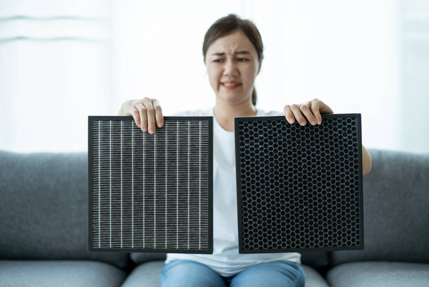 Beautiful Asian young woman holding a HEPA carbon air purifier filter in living room, woman prepare a air purifier filter to be replace the old one. Healthcare and good living lifestyle concept. - Φωτογραφία, εικόνα