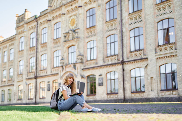 Student at university campus sitting on green grass using laptop - Foto, Imagen