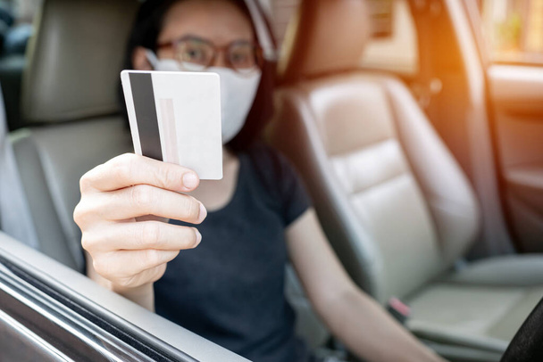 アジアの女性は、カードを使用して高速道路を支払い、頻繁に触れるとサイドカーの背景に表面上の細菌や細菌の汚染、ウイルス保護のための顔をカバーするためにマスクを着用 - 写真・画像