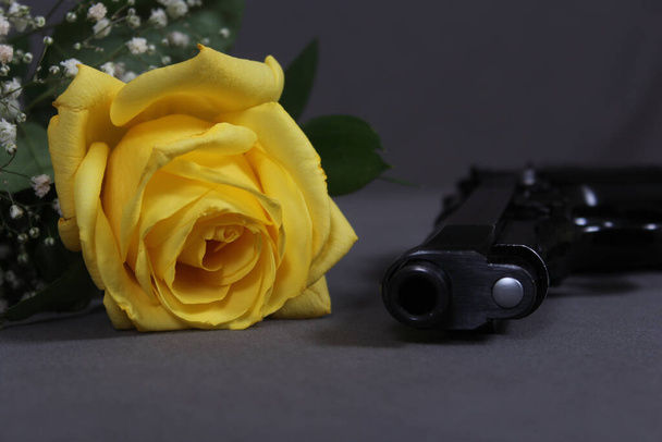 Κίτρινο τριαντάφυλλο στο τραπέζι με μαύρο πιστόλι - Φωτογραφία, εικόνα