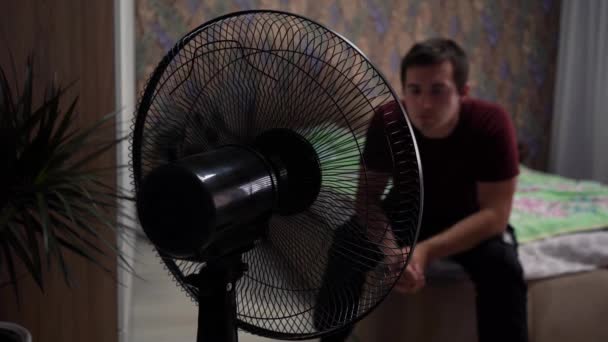 un uomo seduto davanti a un ventilatore nella stanza - Filmati, video