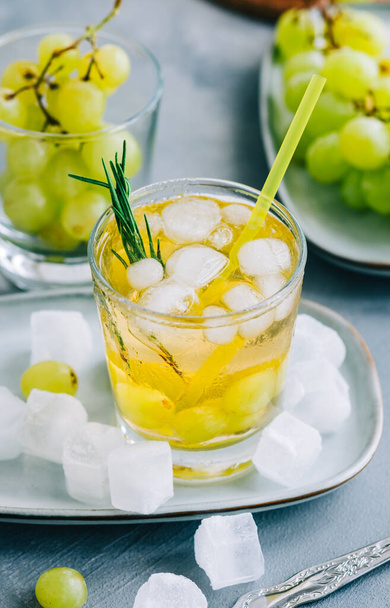 Refreshing summer drink in glass with ice cubes, green grape and rosemary on the table. - Foto, Imagem