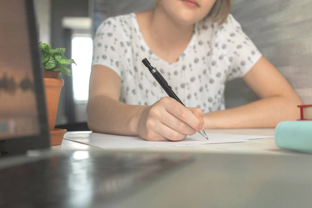 Mladá studentka drží tužku a píše. Vzdělávací koncepce pozadí. Dřevěný stůl s notebookem a pracovním prostorem  - Fotografie, Obrázek