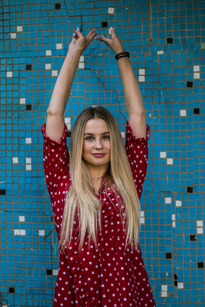 Attractive pretty European female model. Young beautiful blonde woman in a red dress in a white circle on a background of a blue wall. Natural soft evening light. - Fotó, kép